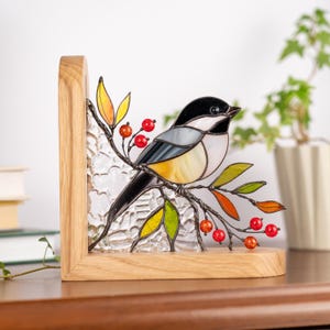 Decorative stained glass chickadee resting on bookshelf.