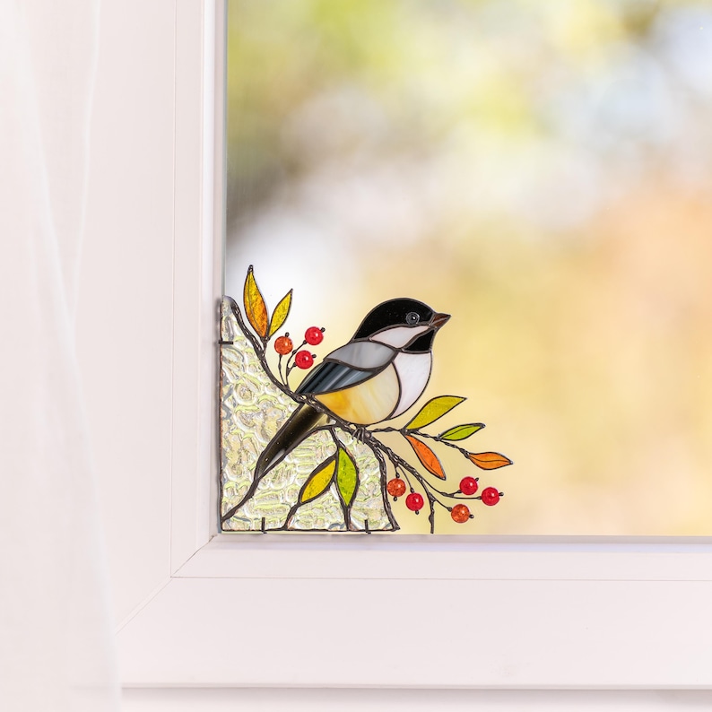 Handmade chickadee ornament perched on leafy branch in glass as a window corner