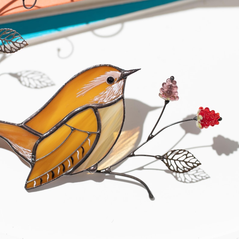 Close up of handmade carolina wren bird stained glass suncatcher, detailed glass feathers and decorative flower branch on white background.