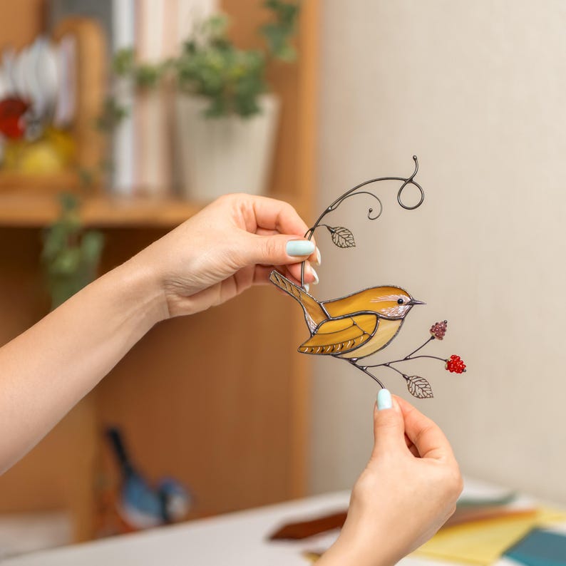 Hands holding stained glass Carolina Wren suncatcher indoors, handcrafted bird window hanging with floral accents.