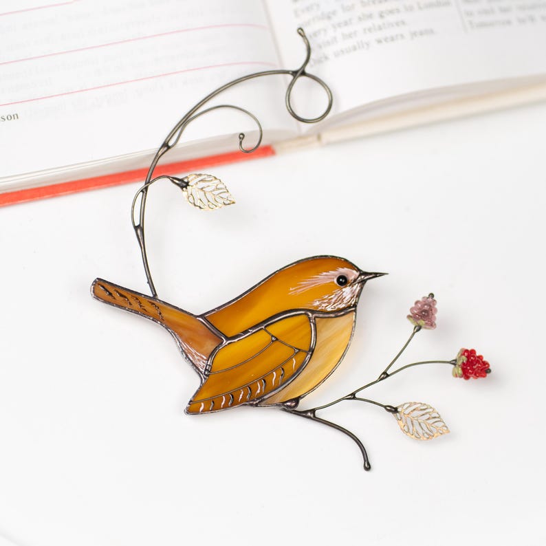 Handmade Carolina Wren stained glass ornament resting on open notebook, delicate floral branch and bird decor.