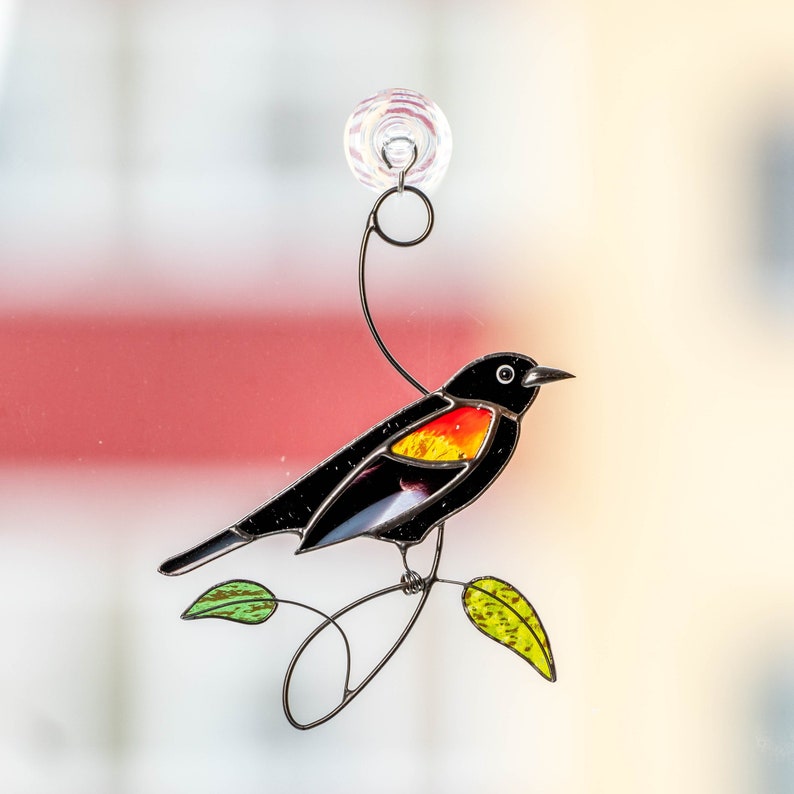 Red winged blackbird sitting on the wire branch with green leafs stained glass lightcatcher