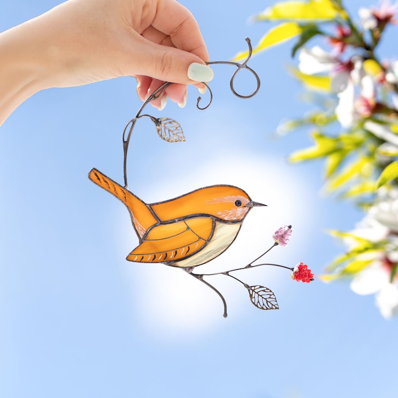 carolina wren stained glass suncatcher held against blue sky background, handmade bird ornament with pink flower accents.