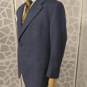 May include: A blue suit with a white collared shirt and patterned tie. The jacket has a two-button closure and a chest pocket. The suit is displayed on a mannequin.