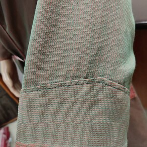 May include: Close-up of a green and pink striped fabric with a folded edge. The fabric has a fine, woven texture.