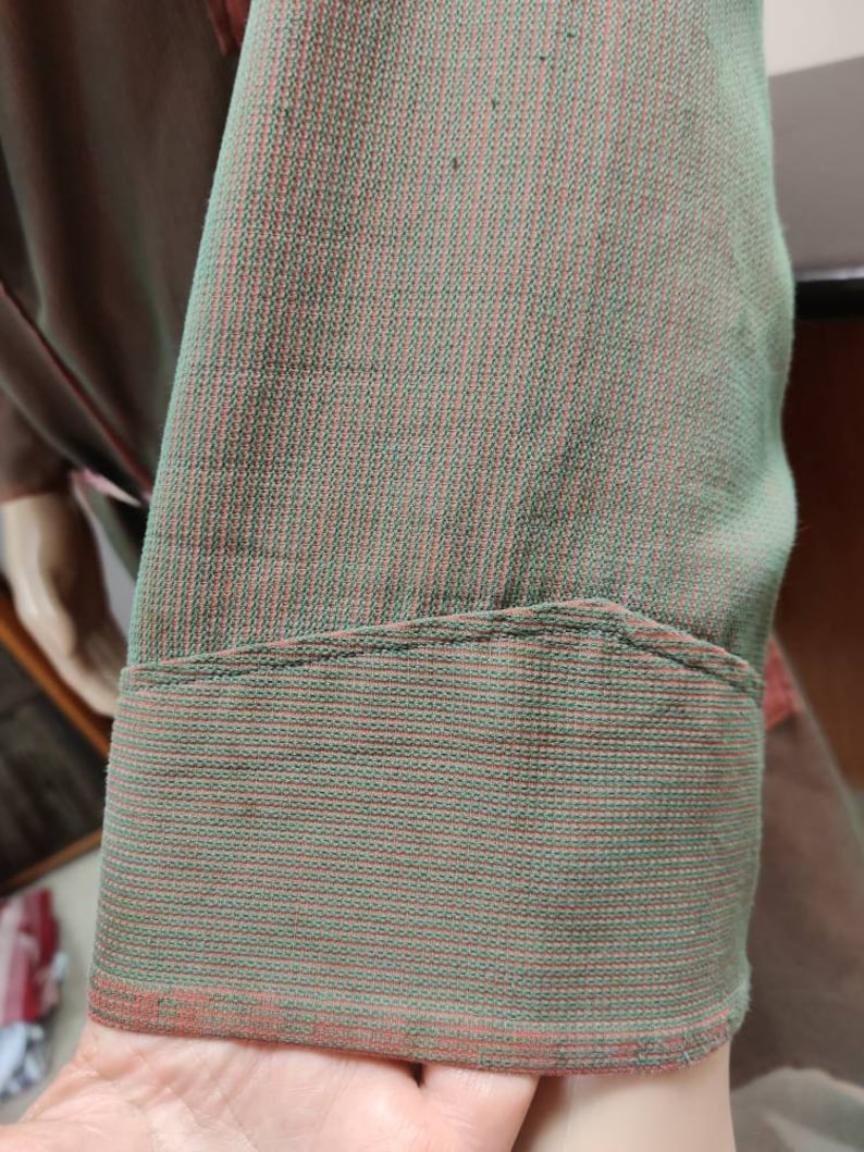 May include: Close-up of a green and pink striped fabric with a folded edge. The fabric has a fine, woven texture.