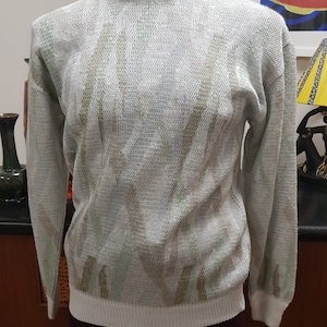 May include: A white sweater with a green and white pattern. The sweater has a crew neck and long sleeves.