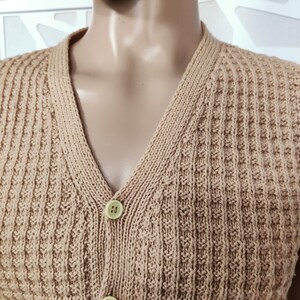 May include: A sleeveless knitted vest with a V-neck and button closure. The vest is a light brown color and has a waffle knit texture.
