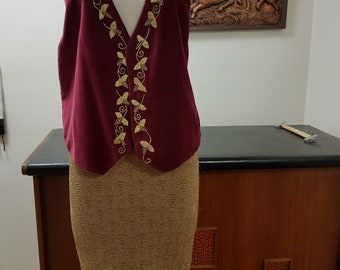 May include: A burgundy velvet vest with gold embroidery of leaves and vines. The vest is paired with a gold skirt with a geometric pattern.