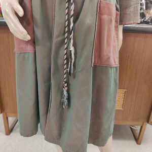 May include: A long, green and pink robe with a black and white rope belt. The robe has a patch pocket on the right side.