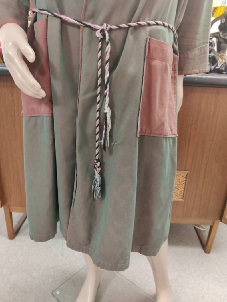 May include: A long, green and pink robe with a black and white rope belt. The robe has a patch pocket on the right side.