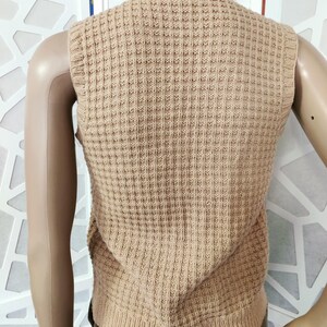 May include: A beige knitted sleeveless vest with a waffle texture.