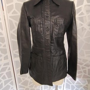 May include: A black leather jacket with a collared neckline and button-up front. The jacket has two chest pockets and two lower pockets. The jacket is displayed on a mannequin.