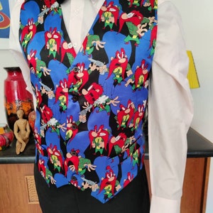 Peut inclure: Un gilet noir avec un fond bleu et un motif répété d'un personnage de dessin animé avec une barbe rouge et un pistolet. Le personnage porte une chemise verte et un chapeau marron.