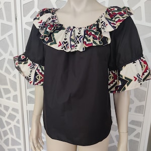 May include: Black blouse with a ruffled neckline and short sleeves. The neckline and sleeves feature a colourful geometric print.