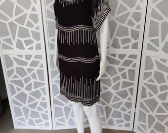 May include: A black short-sleeved dress with a beaded design. The dress has a round neckline and a sheer overlay on the sleeves.