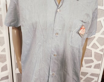 Peut inclure: Une chemise boutonnée à manches courtes bleu clair avec un motif à carreaux blanc et bleu clair. La chemise a une poche sur le côté gauche avec une petite étiquette qui dit "Hawaiian King".