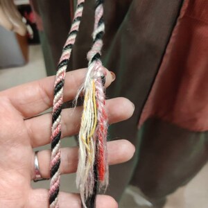 May include: Two black, white, and pink braided cords with frayed ends. The cords are held in a hand.