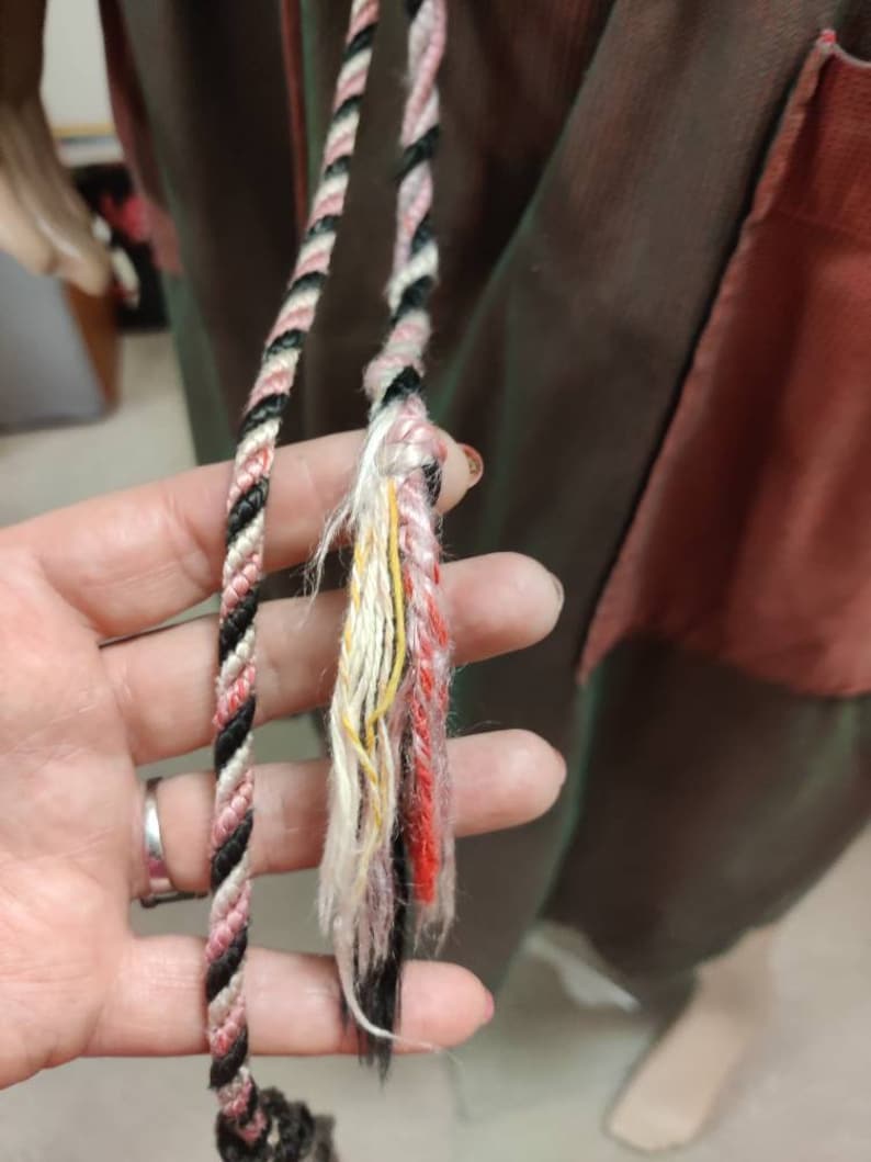 May include: Two black, white, and pink braided cords with frayed ends. The cords are held in a hand.
