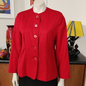 Op de afbeelding: Een rode blazer met een mandarijnkraag en vijf rode knopen. De blazer heeft lange mouwen en een aansluitende pasvorm.