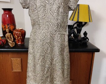 May include: A gold and black brocade dress with a scoop neck and short sleeves. The dress is fitted and has a straight skirt.
