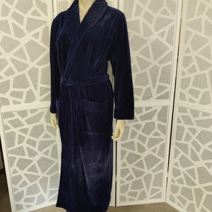 May include: A long, dark blue velour robe with a shawl collar and a tie belt. The robe has a patch pocket on the left side.