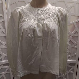 May include: A light green, vintage-style nightgown. The nightgown features a round, embroidered neckline, button-down front, and long sleeves. The fabric appears to be a soft, lightweight material, perfect for sleepwear.