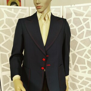 May include: A navy blue blazer with red stitching and red buttons. The blazer has a single button closure and a pocket on the left side.