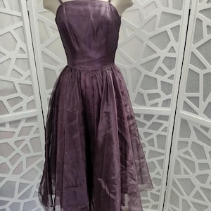 Pode incluir: Um vestido de tule roxo vintage com um corpete justo e uma saia cheia. O vestido tem um decote quadrado e alças finas.
