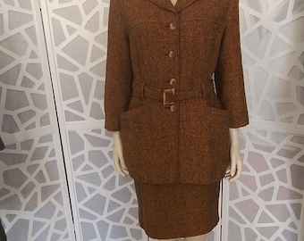 Può includere: Un tailleur gonna in tweed marrone esposto su un manichino. Il completo include un blazer con colletto a revers, chiusura con bottoni e cintura. La gonna abbinata è lunga fino al ginocchio. Il completo è realizzato in tessuto strutturato.