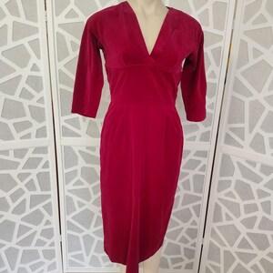 May include: A rich red dress with a V-neck and three-quarter sleeves, displayed on a mannequin. The dress has a tailored fit and a knee-length hem. The fabric looks soft and velvety. The dress is a vintage style.