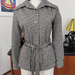 Könnte beinhalten: Grau gesprenkelte Jacke mit passendem Gürtel, auf einer Schaufensterpuppe präsentiert. Die Jacke hat einen Kragen, lange Ärmel und Knopfverschlüsse. Der Stoff hat ein gesprenkeltes Muster aus Grau, Schwarz und Weiß.