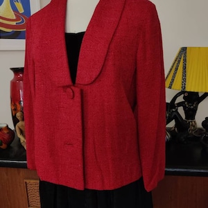 May include: A red wool blazer with a wide collar and a single button closure. The blazer has a textured surface and is displayed on a mannequin.