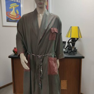May include: A long-sleeved robe with a dark green and brown color gradient. The robe has a shawl collar, a tie belt, and two large patch pockets on the front. The pockets are a contrasting burgundy color.
