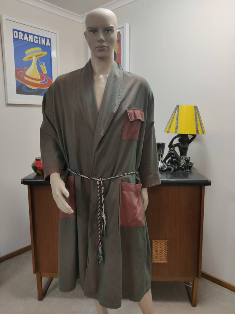 May include: A long-sleeved robe with a dark green and brown color gradient. The robe has a shawl collar, a tie belt, and two large patch pockets on the front. The pockets are a contrasting burgundy color.