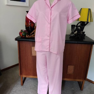May include: A pink pajama set with red trim. The top has a collar and short sleeves. The pants have a straight leg.