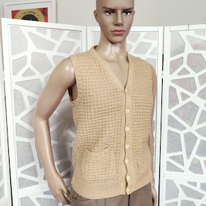 May include: A beige knitted sleeveless vest with a V-neck and button closure. The vest has two pockets on the front.