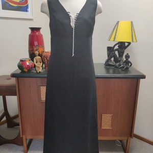 May include: A black maxi dress with a white lace-up detail at the neckline. The dress is sleeveless and has a simple, elegant design.