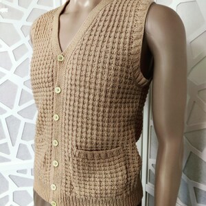 May include: A brown knitted vest with a V-neck and button closure. The vest has two patch pockets and a waffle-like texture.