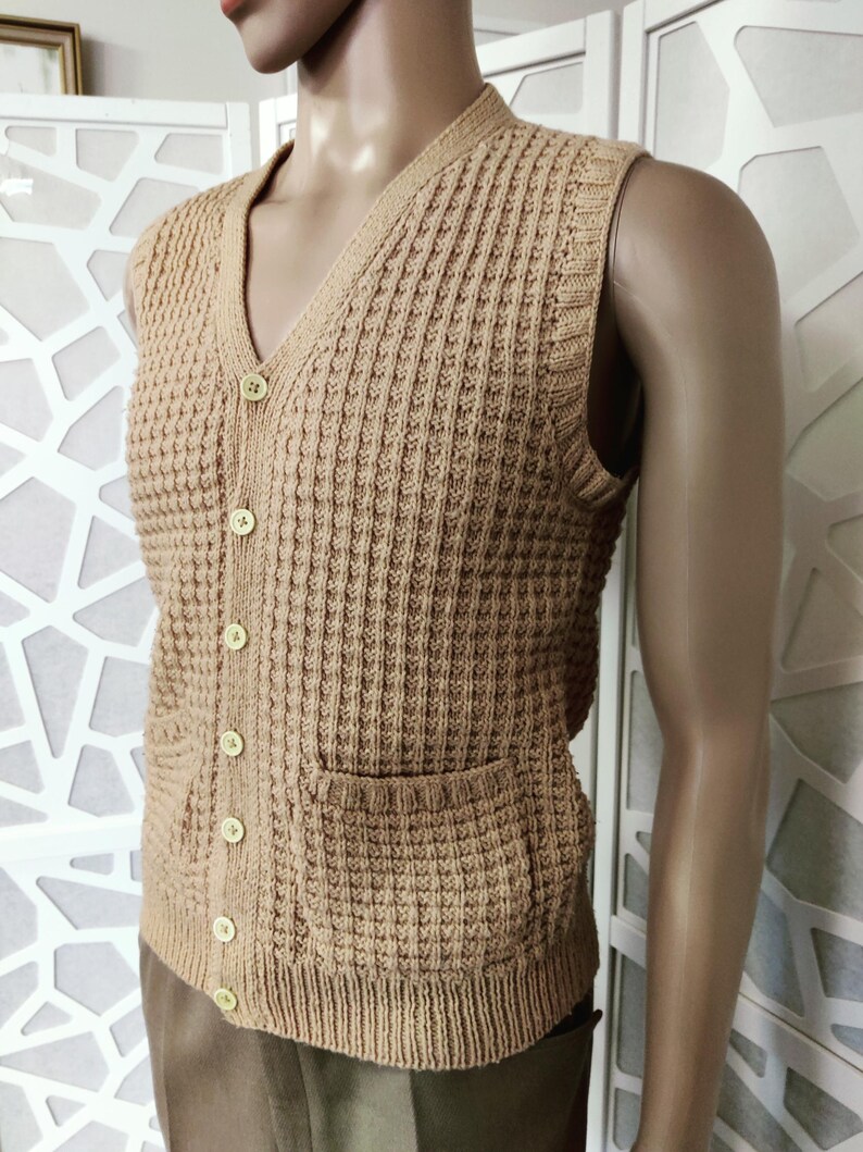 May include: A brown knitted vest with a V-neck and button closure. The vest has two patch pockets and a waffle-like texture.