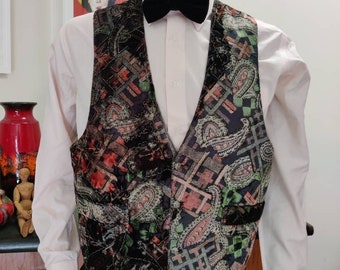 May include: A black velvet vest with a paisley pattern in shades of red, green, and gold. The vest has a V-neck and a button closure.