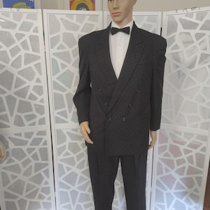 May include: A dark gray double-breasted suit with a subtle pattern, worn by a mannequin. The suit includes a matching jacket, trousers, a white dress shirt, and a black bow tie. The mannequin stands in front of a white decorative screen.