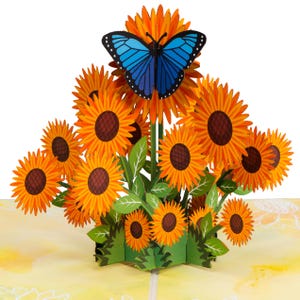 May include: A 3D pop-up card featuring a blue butterfly perched on a bouquet of yellow sunflowers. The card is made of paper and has a delicate, intricate design.
