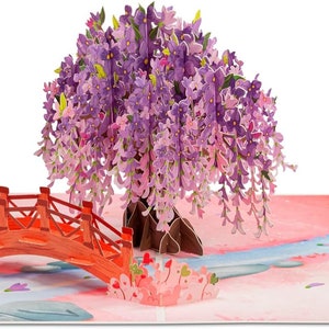 May include: A 3D pop-up greeting card featuring a Japanese garden scene. The card depicts a vibrant purple wisteria tree, a red bridge, and a flowing blue river. The background is a soft pink watercolor wash.