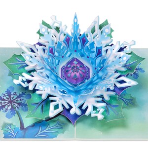 May include: A 3D pop-up card featuring a blue and white snowflake with a purple center. The snowflake is surrounded by green leaves and a blue background.