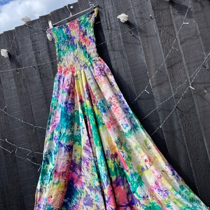 Puede incluir: Un vestido maxi de tie-dye colorido con un escote sin tirantes y una cintura fruncida. El vestido está hecho de una tela ligera y tiene una silueta fluida.