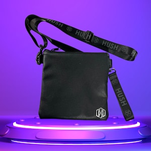 K&ouml;nnte beinhalten: Schwarze Leder-Umh&auml;ngetasche mit einem schwarzen Riemen, auf dem das Wort "HUSH" in Grau gedruckt ist. Die Tasche hat ein silbernes Logo auf der Vorderseite.