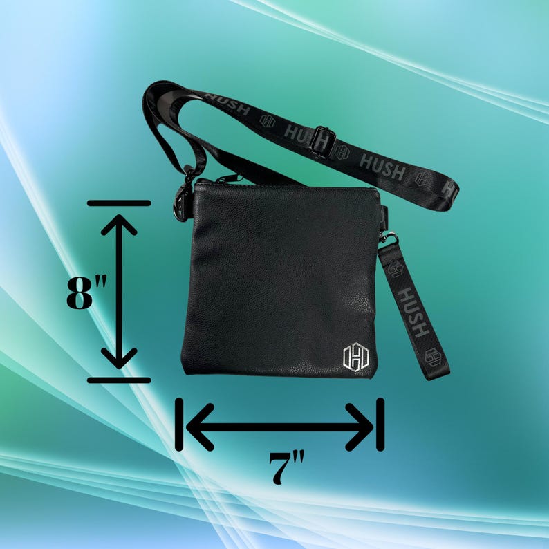 K&ouml;nnte beinhalten: Schwarze Umh&auml;ngetasche mit Rei&szlig;verschluss und einem Riemen mit der Aufschrift "Hush" in wei&szlig;en Buchstaben. Die Tasche ist 17,8 cm breit und 20,3 cm hoch.