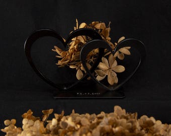 May include: Two black metal heart-shaped frames with dried flowers in the center. The frames are on a black surface.