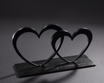May include: Two black metal hearts intertwined, standing on a black base with the inscription "Nick & Tristan".